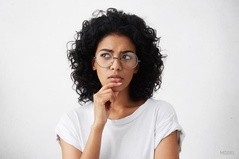 Woman in white shirt, thinking and pondering questions with her hand on her chin.