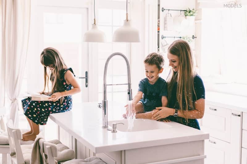 Mother with her children playing with water in kitchen sink at home.