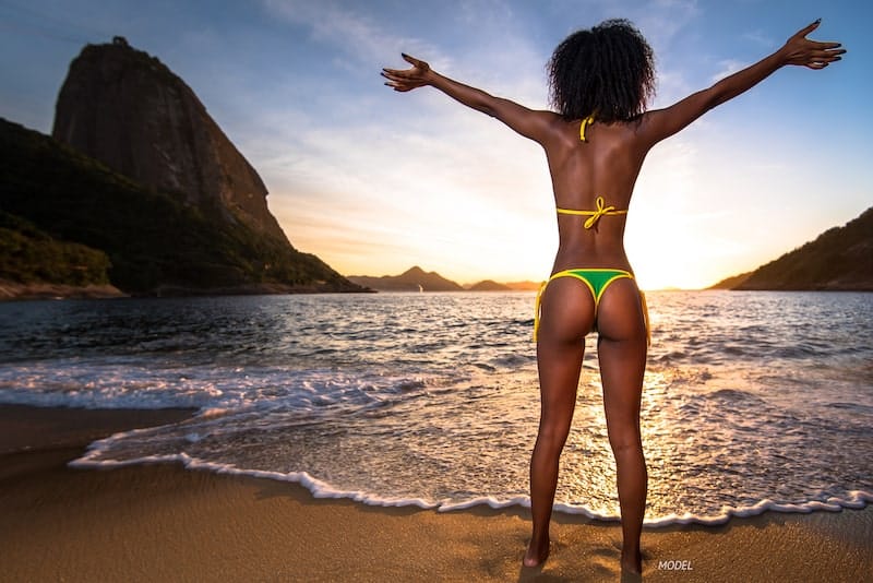 Thin, African American woman in a bikini standing on beach, showing her buttocks