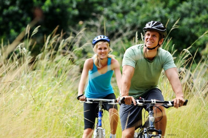 Happy couple riding bikes together with trees and high grass around them